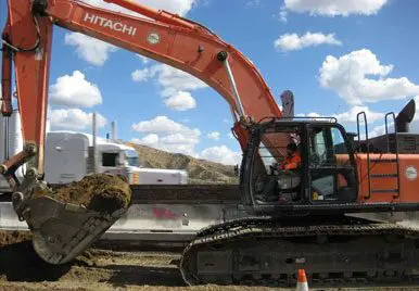A large orange and black excavator on the side of road.